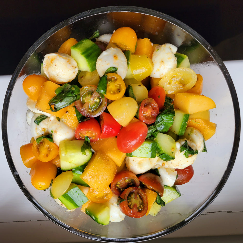 Colorful salad with tomatoes, cucumbers, and mozzarella in a glass pyrex bowl.