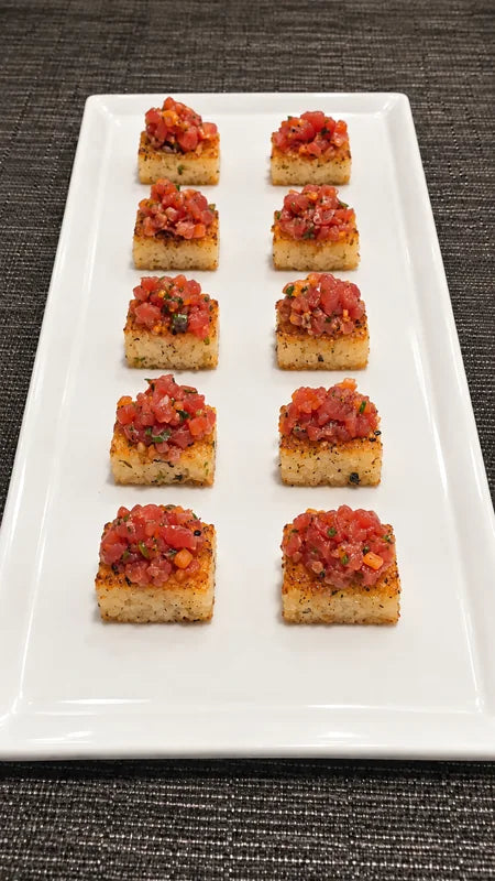 Rows of small golden bites finished with a red topping on a white platter.