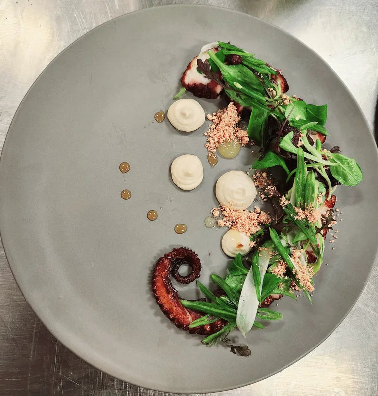 A carefully arranged octopus dish on a large grey plate.