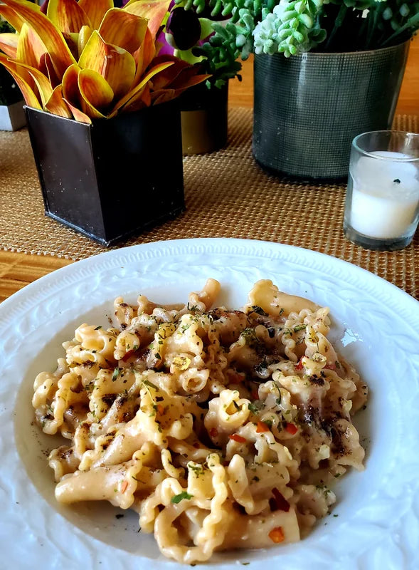 A plate of pasta on a dining table beside flowers and a candle.