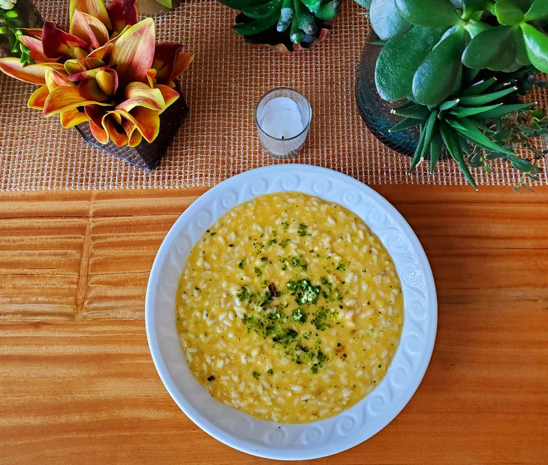 A white plate of risotto on a wooden table with plants and flowers.