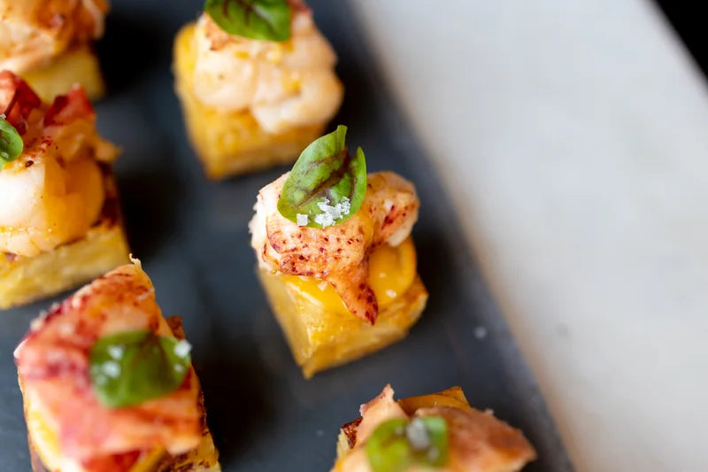 Small lobster-topped bites arranged across a dark serving surface.
