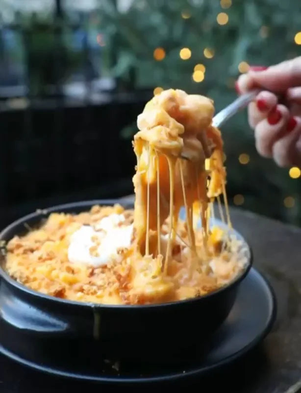 A fork lifting macaroni and melted cheese above a serving dish.