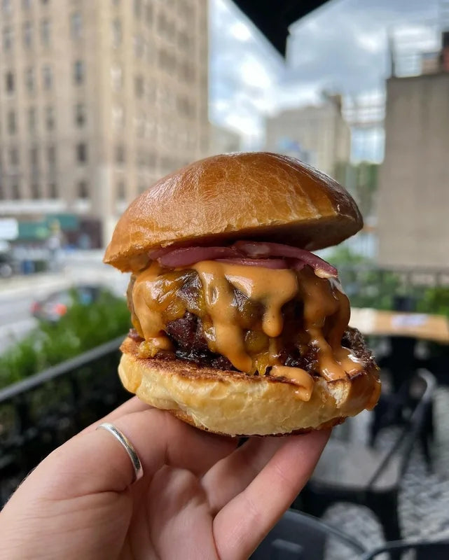 A burger held in one hand in front of a city street.
