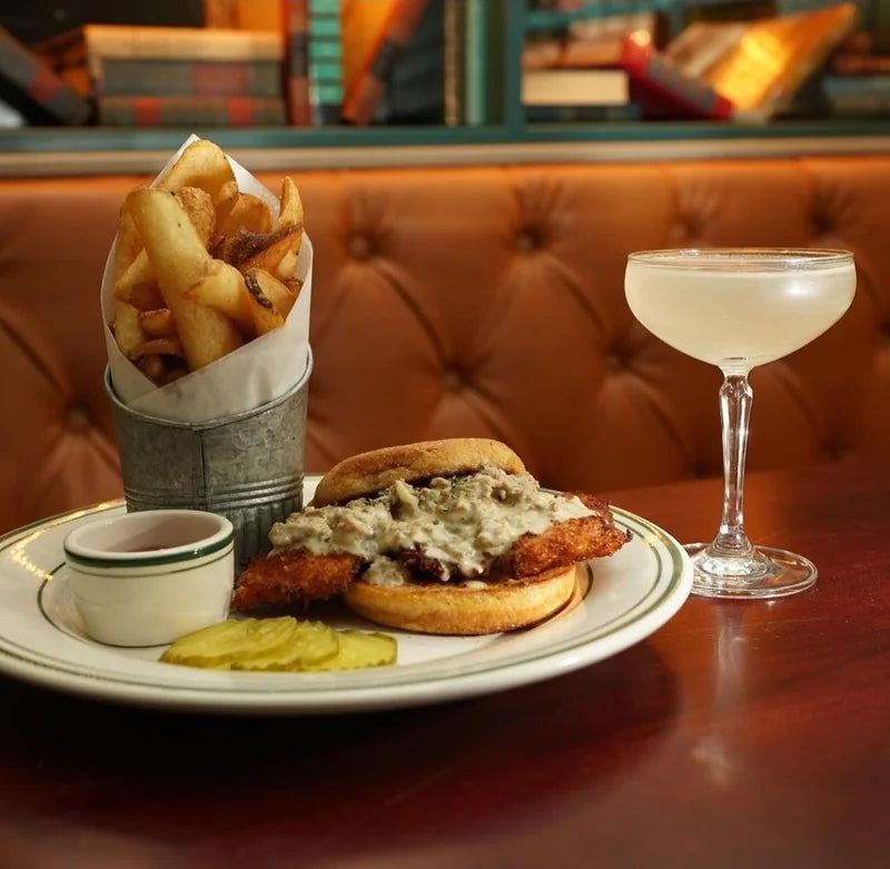 A fried chicken sandwich with fries and a drink on a restaurant table.