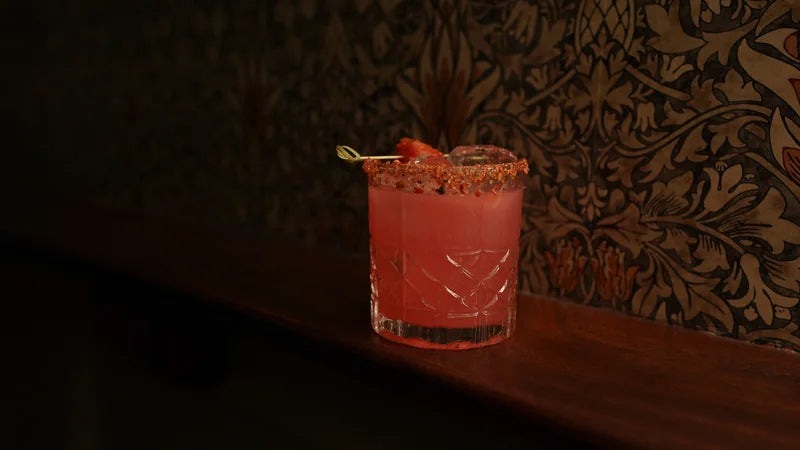 A vivid red drink in a short glass against a dark patterned background.